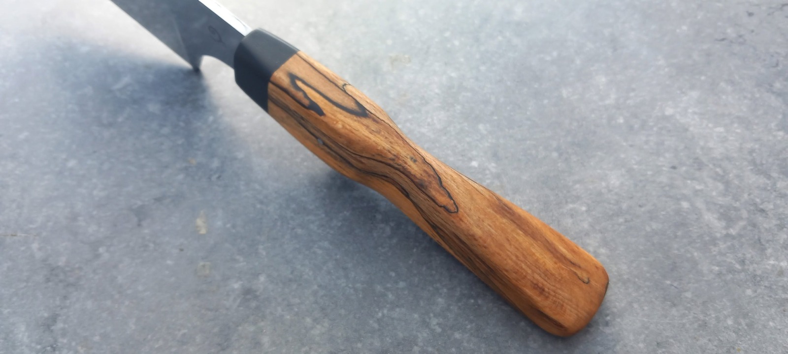 Détail d'un manche en bois spalté et de sa mitre noire sur un couteau de cuisine