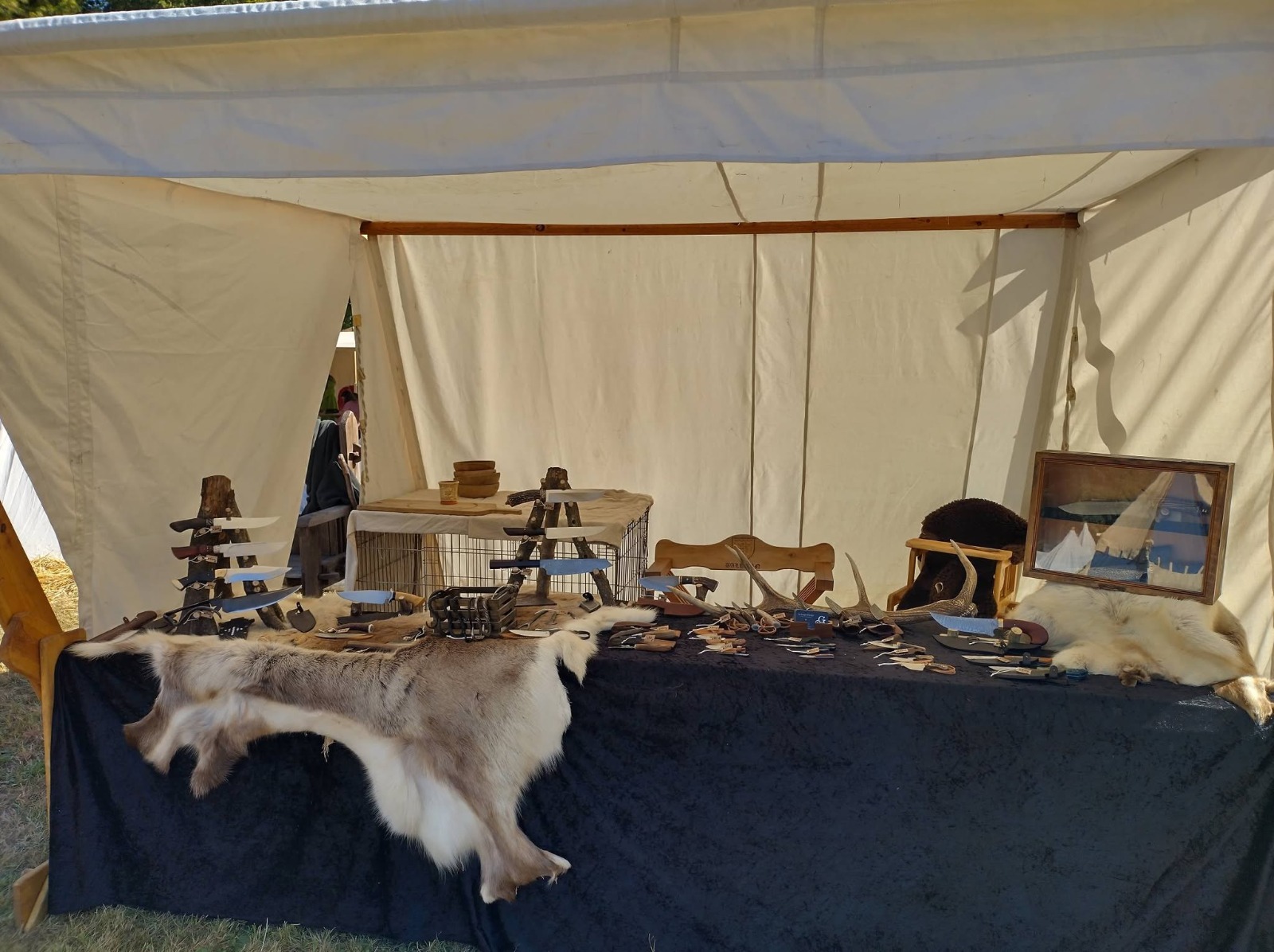 Stand de coutellerie sous tente de toile, couteaux présentés sur peaux et bois de cerf